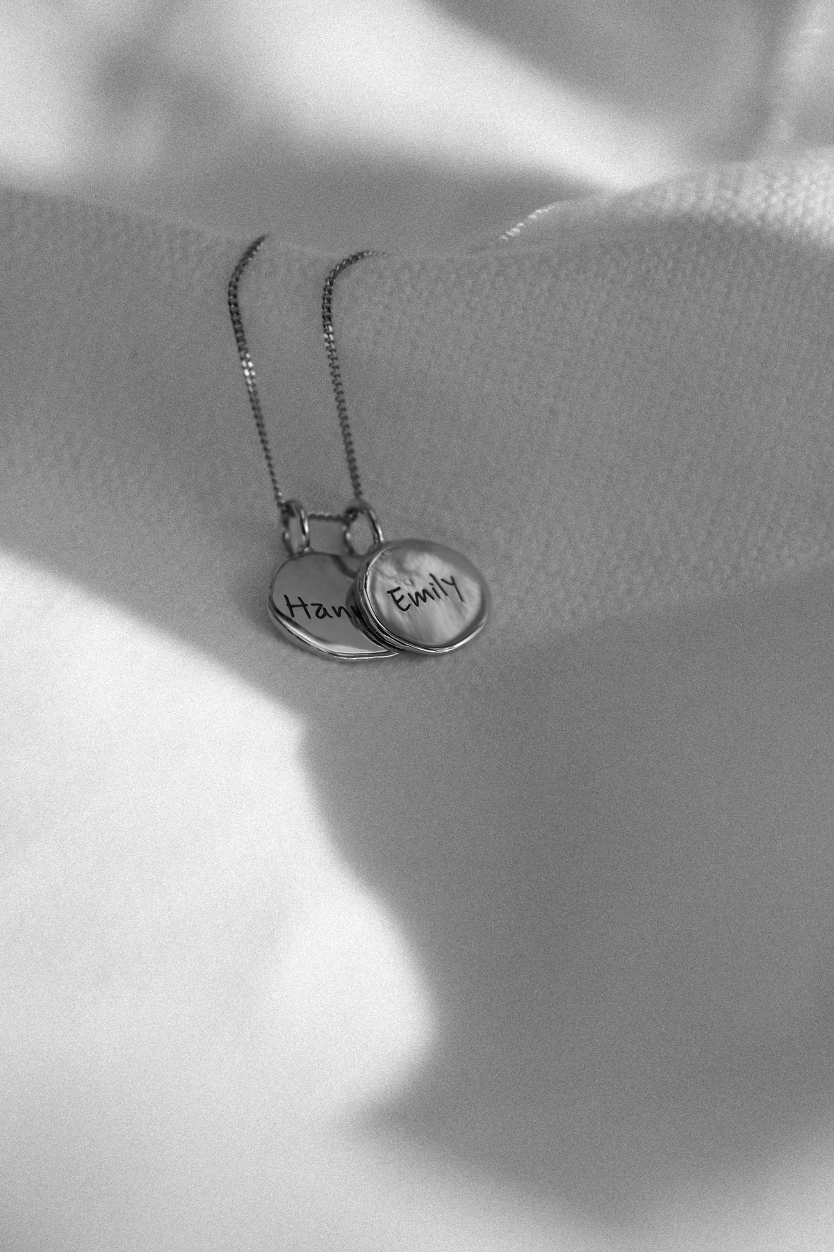 Two silver fingerprint pendants engraved with names, on white fabric