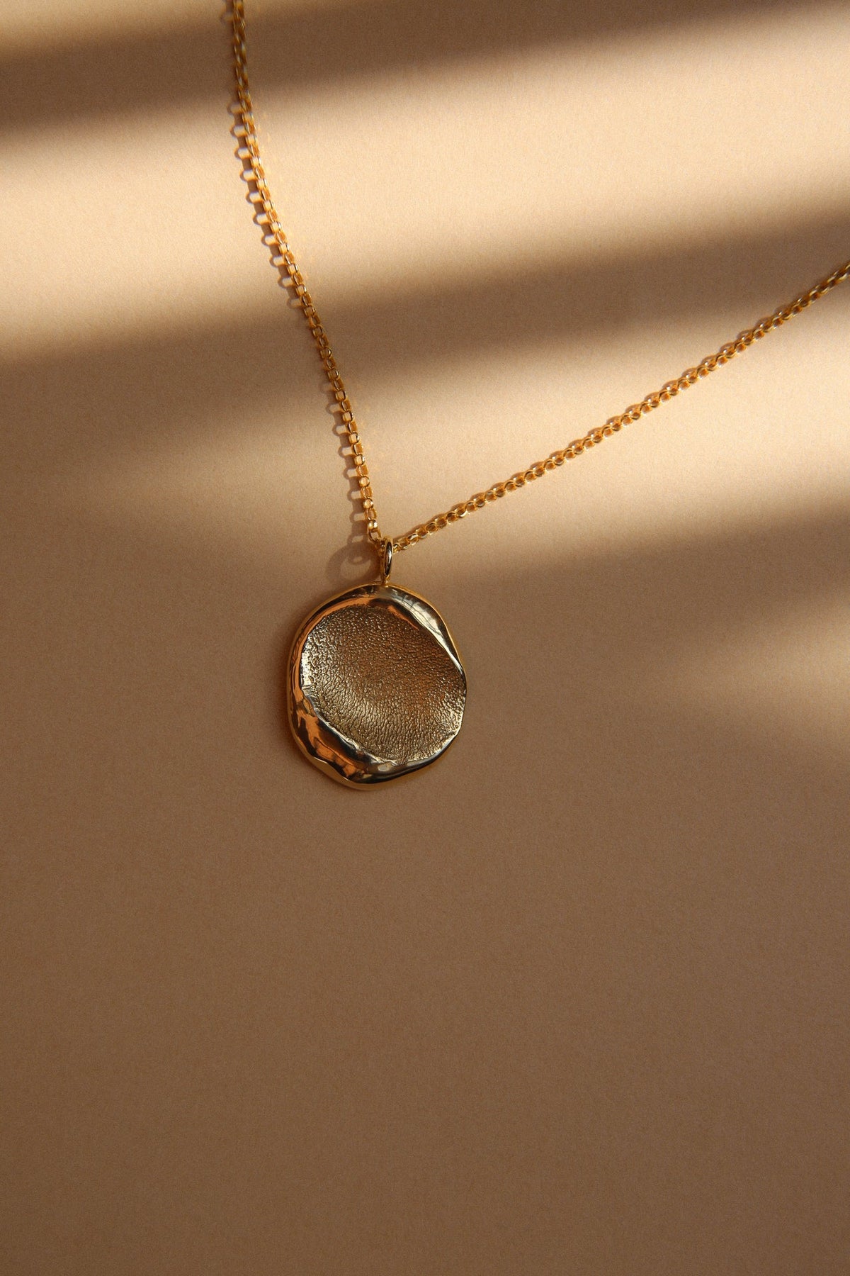 Gold fingerprint pendant on a chain, catching the light